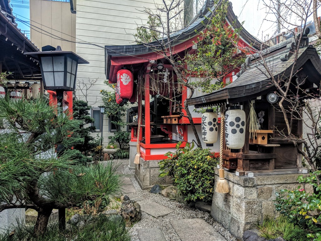 A peaceful traditional Japanese garden featuring a stone pathway, wooden shrines with colorful lanterns, and lush greenery.